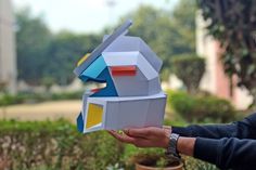 a person holding an object made out of paper in front of some bushes and trees