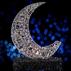 a crystal moon sculpture sitting on top of a black surface with blue lights in the background