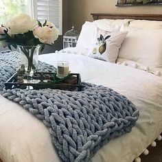 a bed with white sheets and pillows in a bedroom next to a vase filled with flowers