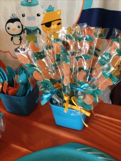 a table topped with blue plates and cups filled with candy bar wrapper bouquets