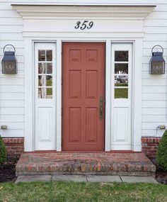 a red front door with two sidelights and brick steps in front of a white house