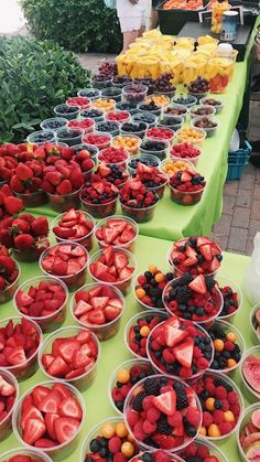 there are many bowls of strawberries and other fruits on the table at this outdoor market