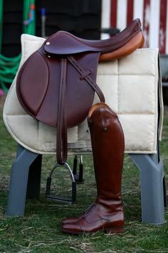 a brown and white horse saddle sitting on top of a green field next to a chair