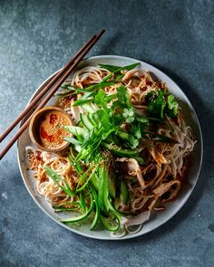 a white plate topped with noodles and veggies next to two chopsticks