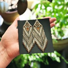 a hand holding a pair of beaded earrings in front of a potted plant