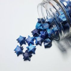 a jar filled with blue stars sitting on top of a white table next to a glass container