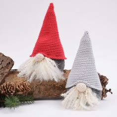 two crocheted gnomes sitting on top of a log next to pine cones