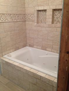 a bath tub sitting inside of a bathroom next to a wooden door and tiled walls