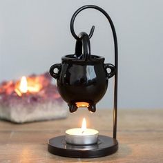 a black tea light holder with a candle in it sitting on a table next to a lit candle