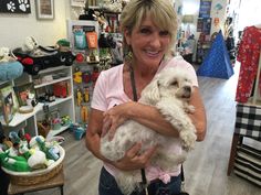 a woman holding a white dog in a pet shop with lots of toys on the floor