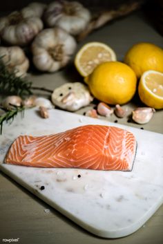 a piece of salmon sitting on top of a cutting board next to lemons and garlic