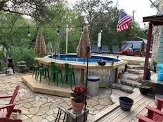 an above ground pool surrounded by patio furniture and umbrellas with flags on the roof