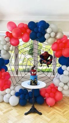 a spiderman birthday party with balloons, cake and balloon arch in the shape of a web