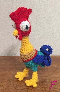 a crocheted chicken is standing on a table with its head turned to the side