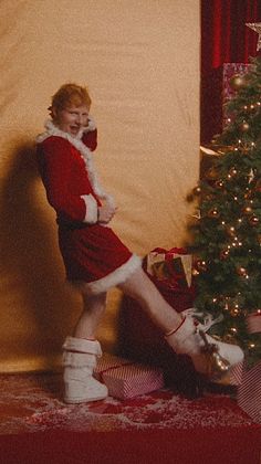 a woman dressed as santa clause standing next to a christmas tree