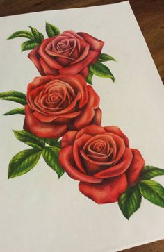 a drawing of three red roses with green leaves on white paper next to a wooden table