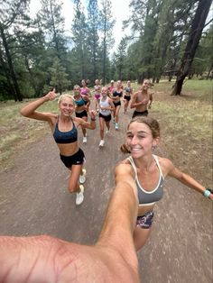 a group of people running down a dirt road in the woods with trees behind them