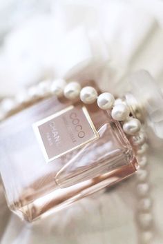 a bottle of perfume sitting on top of a bed next to a beaded necklace