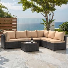 an outdoor patio furniture set with beige cushions and coffee table, overlooking the ocean on a sunny day