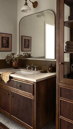 a bathroom sink sitting under a large mirror next to a wooden cabinet filled with towels