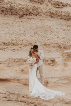 a bride and groom standing on the beach in front of some sand dunes with their arms around each other