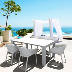 an outdoor dining table and chairs on a deck overlooking the ocean with white drapes