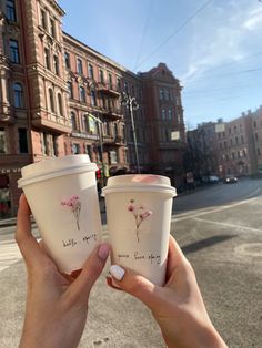 two people holding up coffee cups on the street