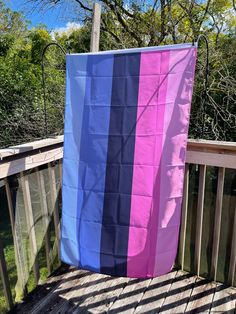 a blue, pink and purple striped towel sitting on top of a wooden deck next to trees