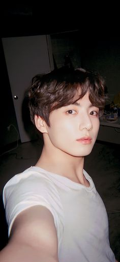 a young man with dark hair and white shirt looking at the camera while standing in a room