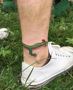 a small tattoo on the ankle of a man's foot with a green alligator