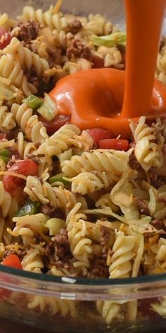 a glass bowl filled with pasta salad and an orange sauce being poured on top of it