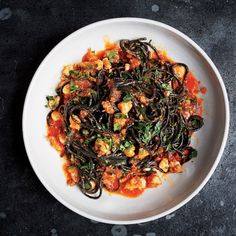 a white plate filled with pasta and vegetables on top of a black tablecloth next to a fork