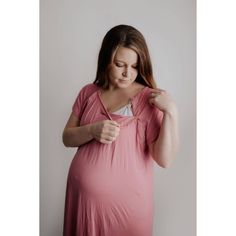 a pregnant woman in a pink dress is holding her hand on her shoulder and looking down