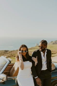 a man and woman standing in front of a car