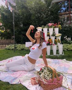 a woman sitting on top of a blanket next to a basket filled with flowers and potted plants