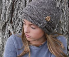 a young woman wearing a knitted hat and looking down at her cell phone in front of a tree