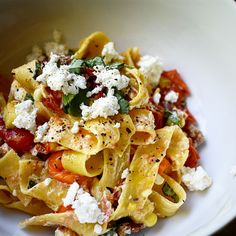 a white bowl filled with pasta covered in fettuccine, tomatoes and parmesan cheese