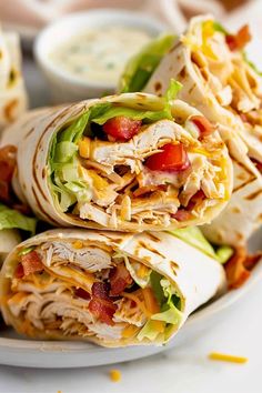 a white plate topped with two wraps filled with chicken and lettuce next to dipping sauce