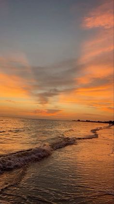 the sun is setting over the ocean with waves coming in to shore and people walking on the beach