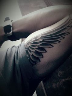 a black and white photo of a man's arm with wings tattooed on it