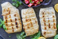 three fish fillets on a plate next to a bowl of vegetables and lemons