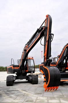 an orange and black construction vehicle parked on top of a cement ground next to another truck