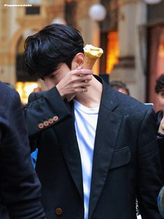 a man holding an ice cream cone to his face while standing in front of other people