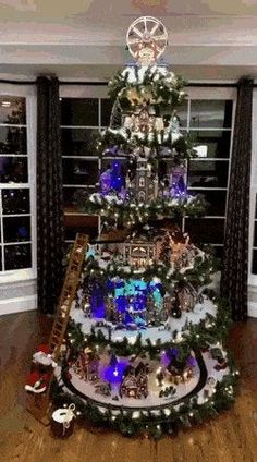 a decorated christmas tree in the middle of a living room with large windows and wooden floors