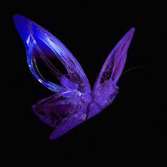 a purple glass butterfly sitting on top of a black surface in the dark, with its wings spread out