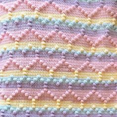 a crocheted blanket that is laying on top of a bed sheet with pink, yellow and blue stripes