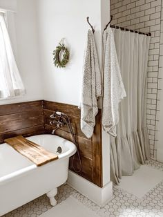 a white bath tub sitting under a window next to a wooden shelf filled with towels