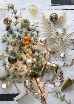 a christmas tree surrounded by ornaments on a white wooden table with pine branches and other holiday decorations