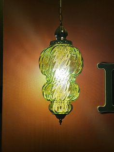 a green glass light hanging from a hook on a wall next to the letter j