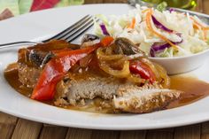 a white plate topped with meat and veggies next to a bowl of coleslaw